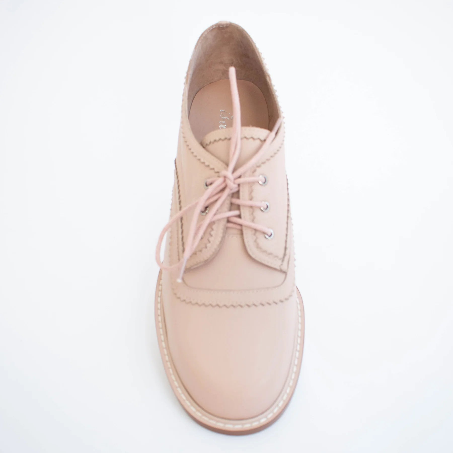 Beige leather shoe with pink laces on a light gray background