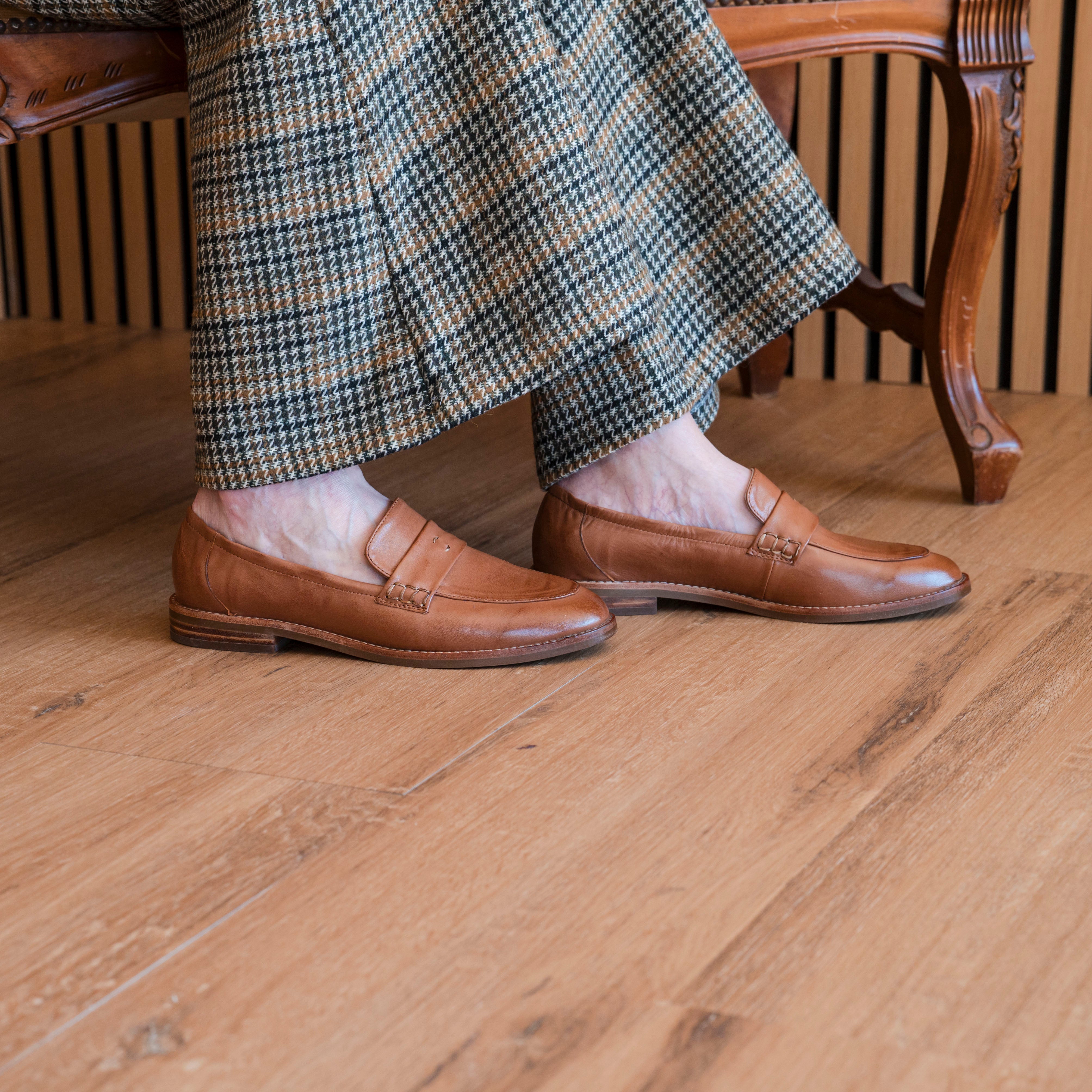 Person wearing brown loafers and plaid pants on a wooden floor.