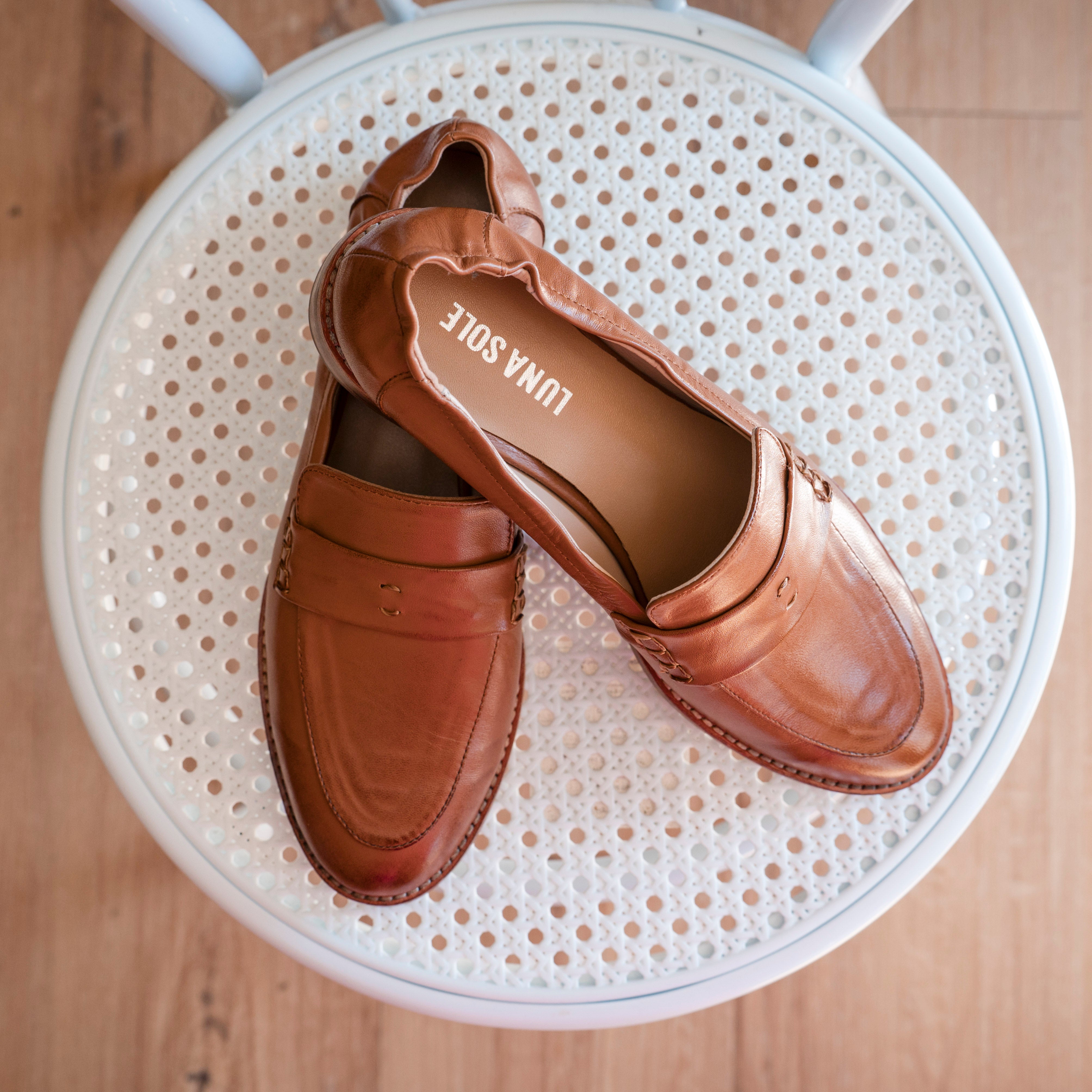Pair of brown loafers on a white chair with 'Lina Sote' branding.