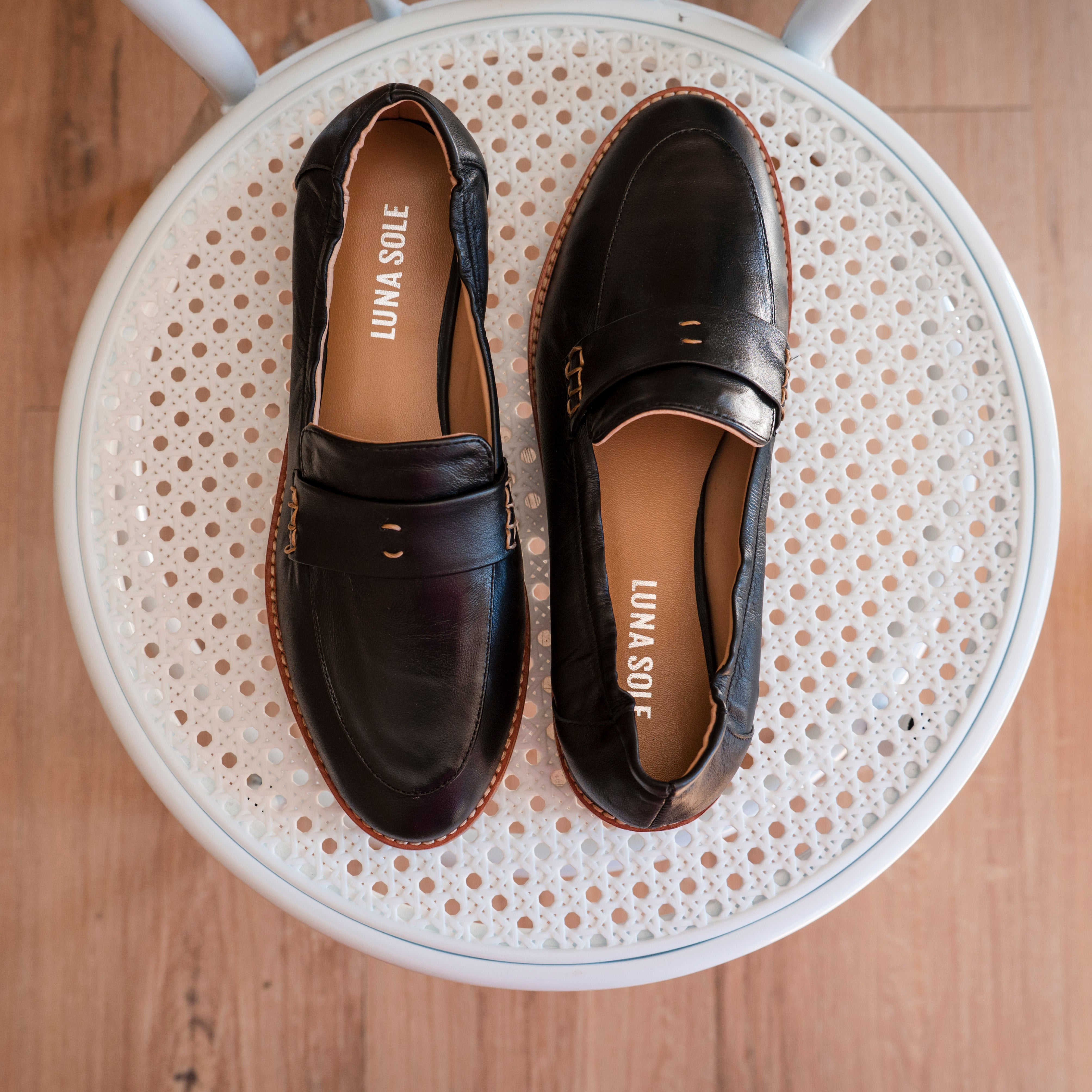 Pair of black loafers on a round white stool with a wooden floor background