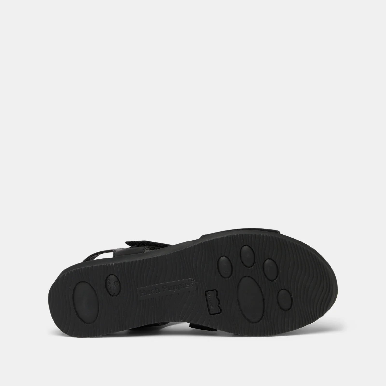The black rubber outsole of a sandal, showing a paw-print pattern and embossed branding, photographed against a light gray background.