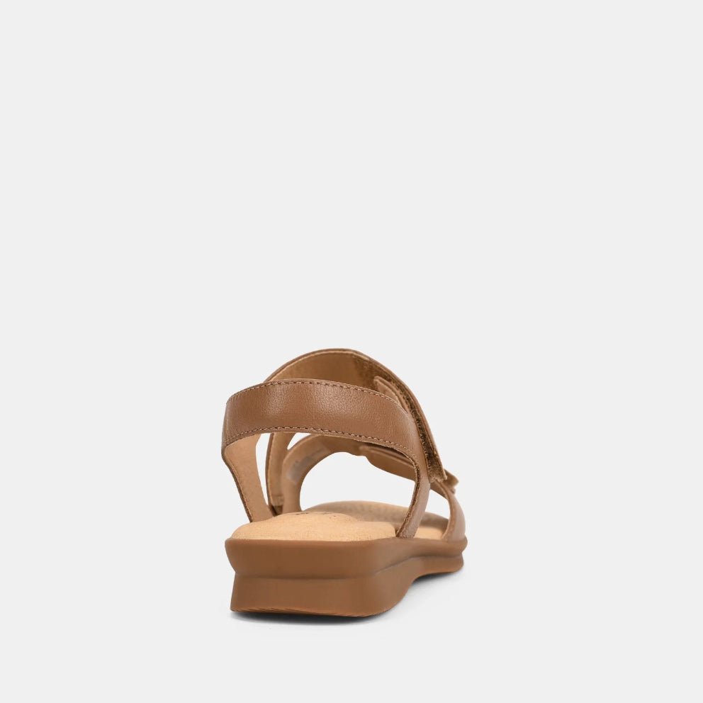 A single tan leather sandal shown from the back, featuring a low wedge heel and a wide crossover strap design, set against a plain light gray background.