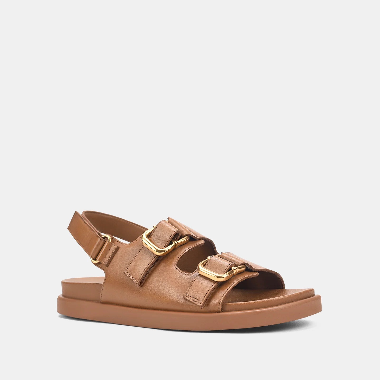 A single tan leather double-strap sandal with gold-tone buckle hardware, shown from a side profile on a light gray background.